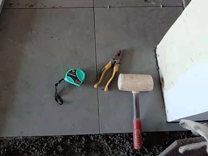 客廳地磚鋪貼：鋪貼的工具包括橡膠錘和粘結(jié)劑。在進(jìn)行施工之前先把所需要的這些材料都整理好放在一旁備用；基層的處理工作對(duì)瓷磚的平整度有很大的影響，對(duì)于基層要做好清潔工作，還有找平工作。放樣：在進(jìn)行瓷磚的鋪貼工作之前還事先找好垂直線，這樣可以在鋪貼的時(shí)候找到瓷磚的水平線，讓瓷磚鋪貼的更加的平整。粘結(jié)劑加水?dāng)嚢杈鶆?，靜置10分鐘之后就可以使用。將瓷磚表面的浮灰清除，再在瓷磚背面均勻的涂抹上粘結(jié)劑，按照預(yù)鋪的順序?qū)⒋纱u鋪貼在地面上，最后用橡膠錘輕輕拍打至服帖齊整。